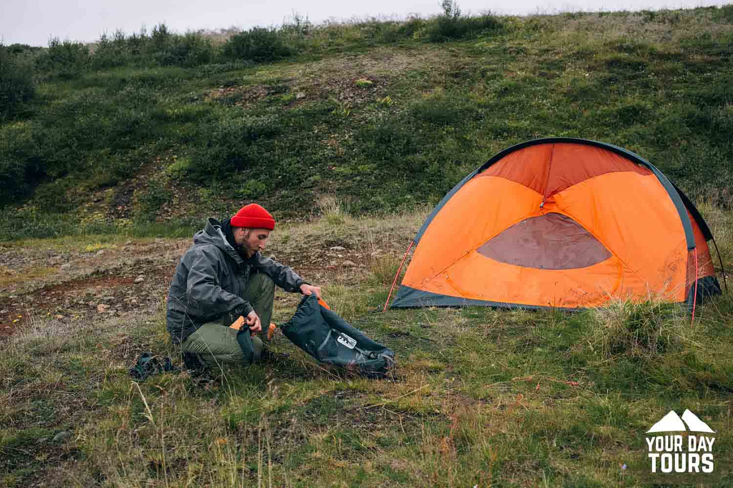 person with an orange tent in green fields