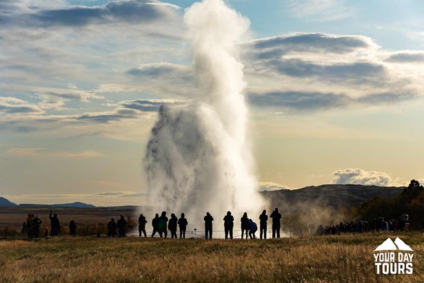 silhouettes of people standing by erupting geysir 