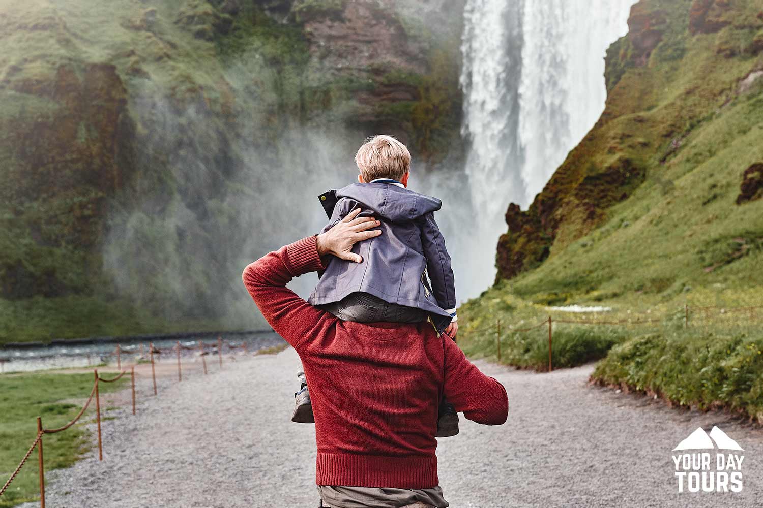 son sitting on father shoulders looking at skogafoss