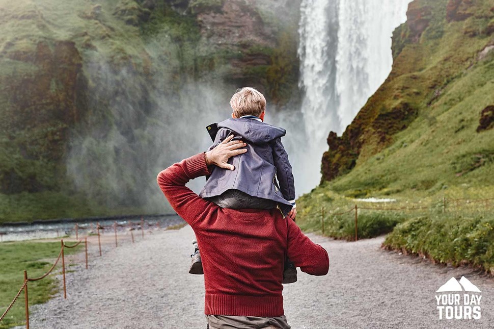 son sitting on father shoulders looking at skogafoss
