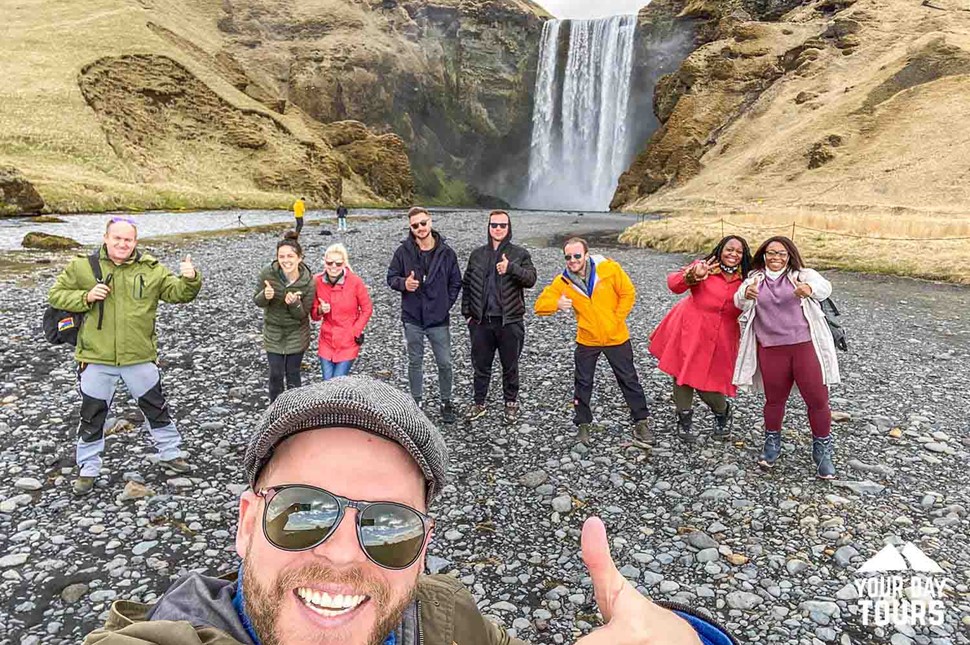 happy group of people taking a slefie by skogafoss waterfall