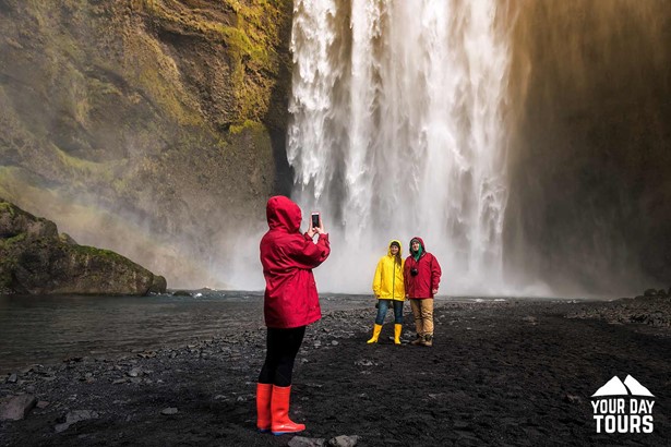 people with raincoats taking pictures in skogafoss