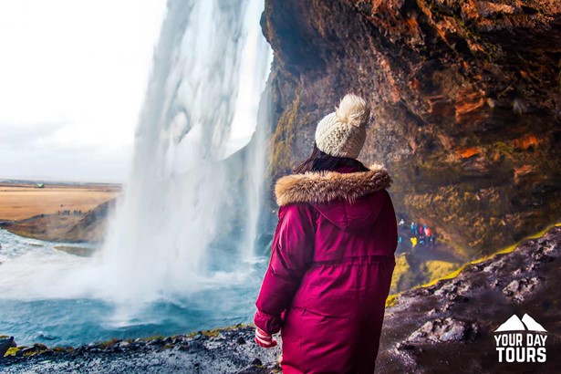 woman in a pink coat and a white hat behind seljalandsfoss