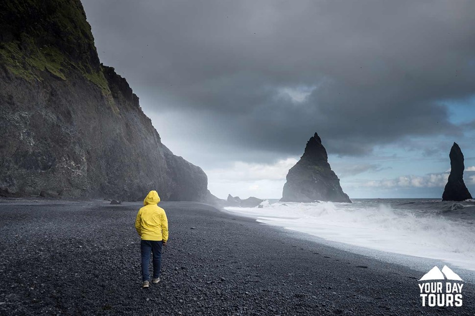 person with a yellow coat at reynisfjara black sand beach 