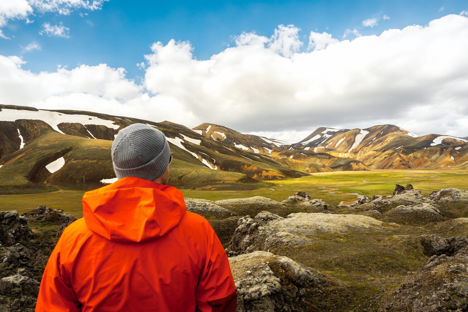 Male in bright red jacket and grey beanie standing in front of Landmannalaugar mountain
