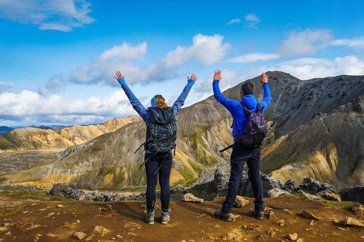Two tourists in blue sweaters waving arms happily hiking on Landmannalaugar tour 