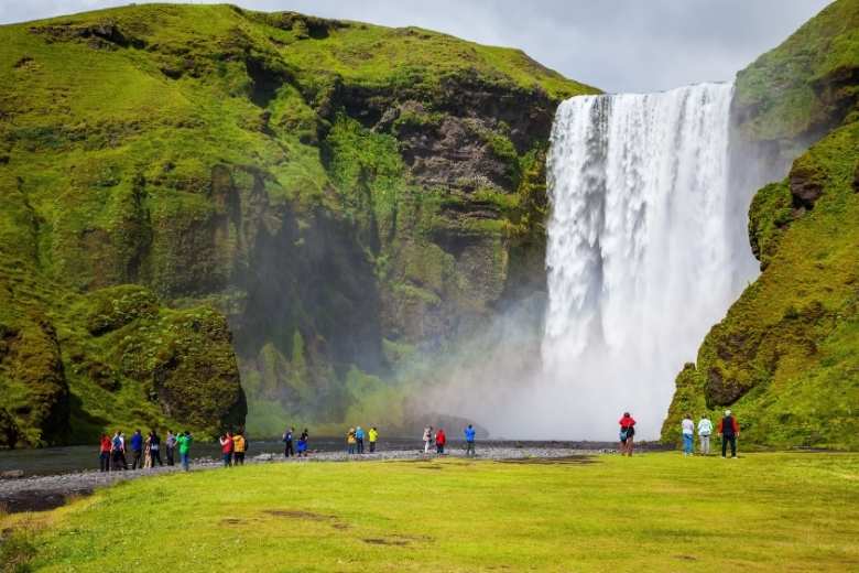 Small tour group walking and admiring view of Skogafoss waterfall in summer.